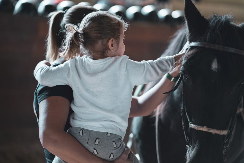 Woman holding child petting a horse at a stable, showcasing gentle bonding and animal interaction.